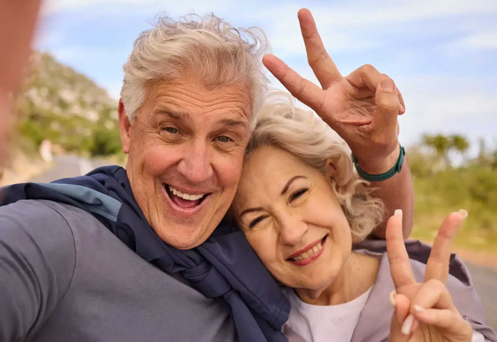 Pareja de ancianos sonrientes mostrando el signo de paz al aire libre, disfrutando de un día soleado.