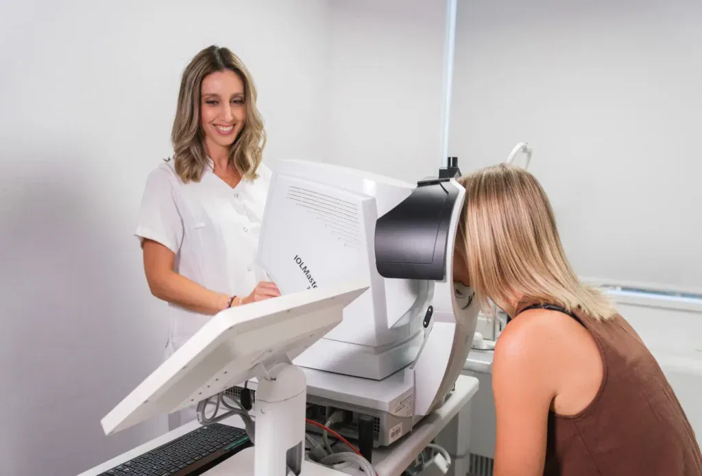 Mujer en consulta oftalmológica, realizando un examen de la vista con un dispositivo especializado, mientras una profesional de la salud la asiste.