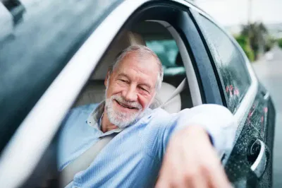 Hombre mayor sonriente asomándose por la ventana de un coche, transmitiendo una sensación de felicidad y tranquilidad.